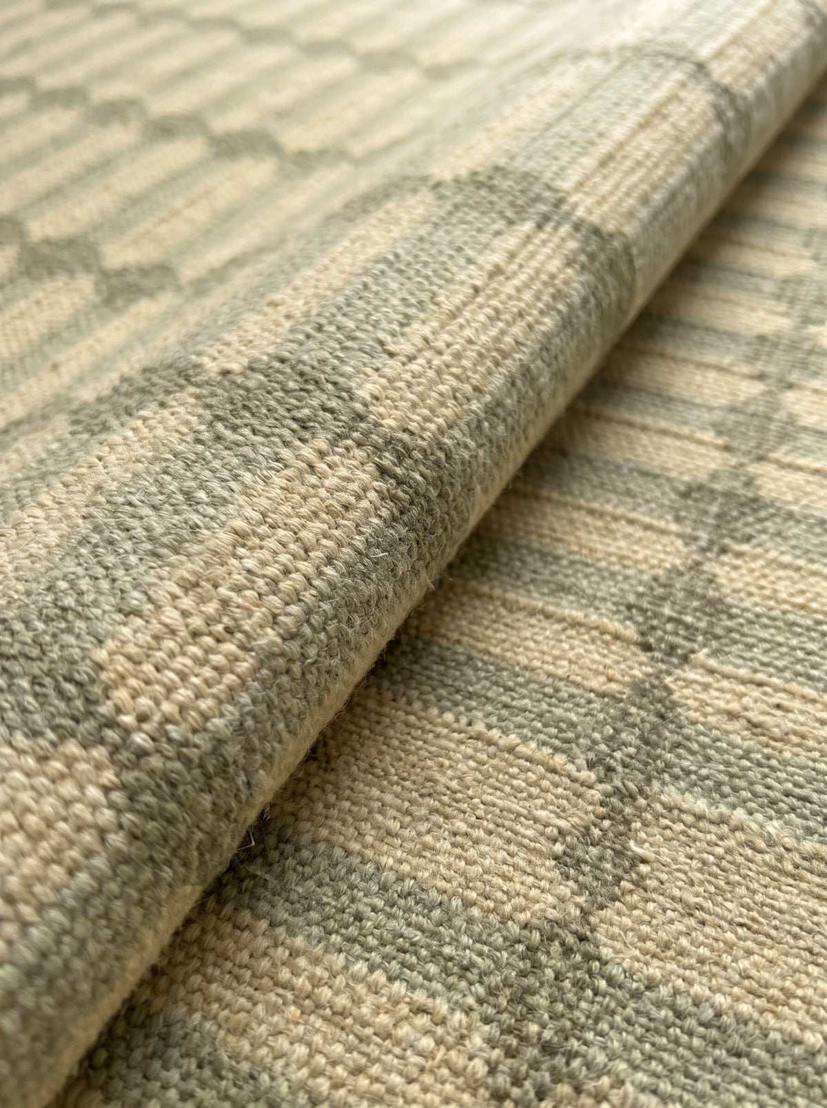 Article 211 sage trellis stripe merino wool flatweave rug folded back to show the weave and texture