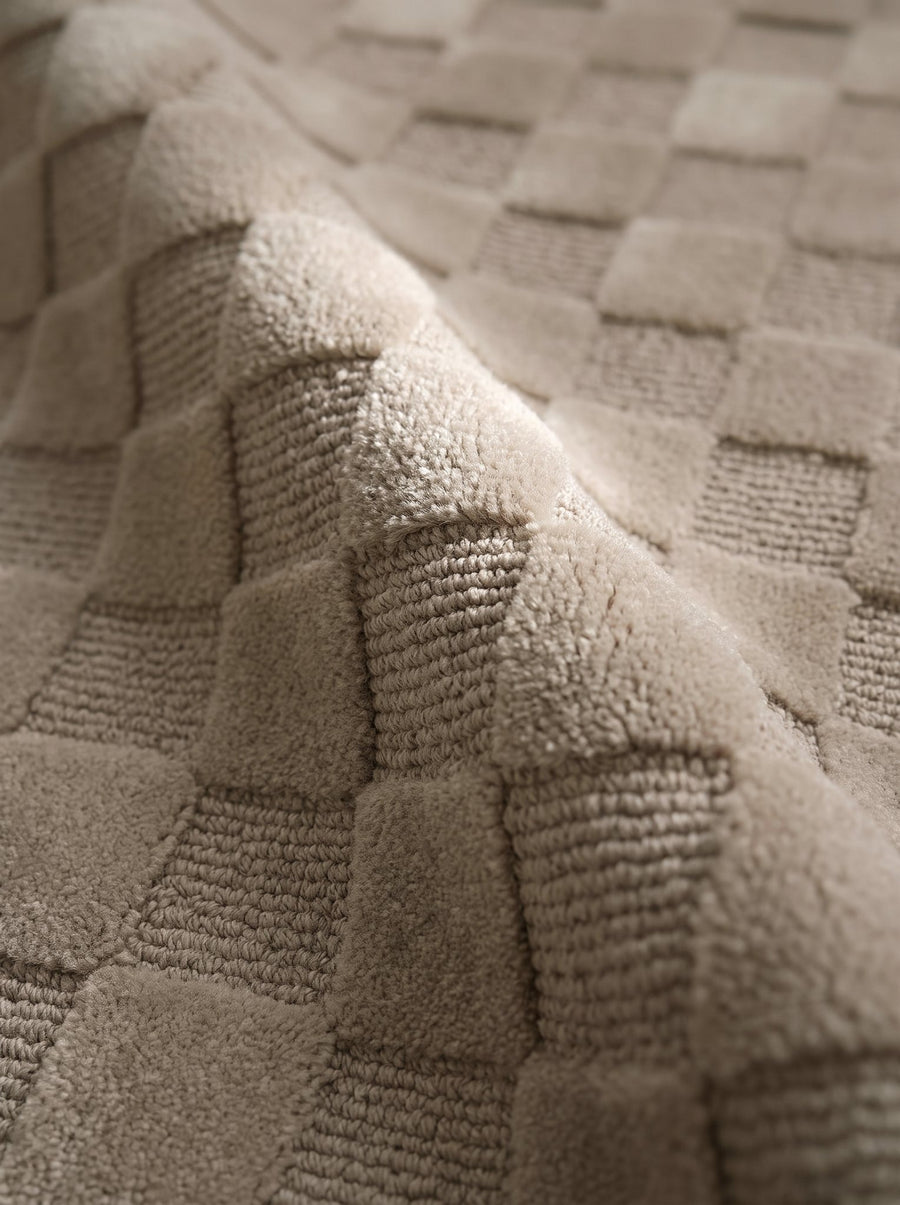 Article 241 taupe checkerboard merino wool and cashmere hand-knotted rug folded back to show pile depth and texture