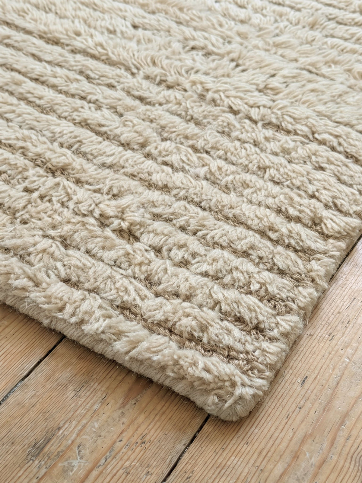 Corner of the Article 411 ivory ribbed texture alpaca and linen handwoven rug showing the pile and finished edge