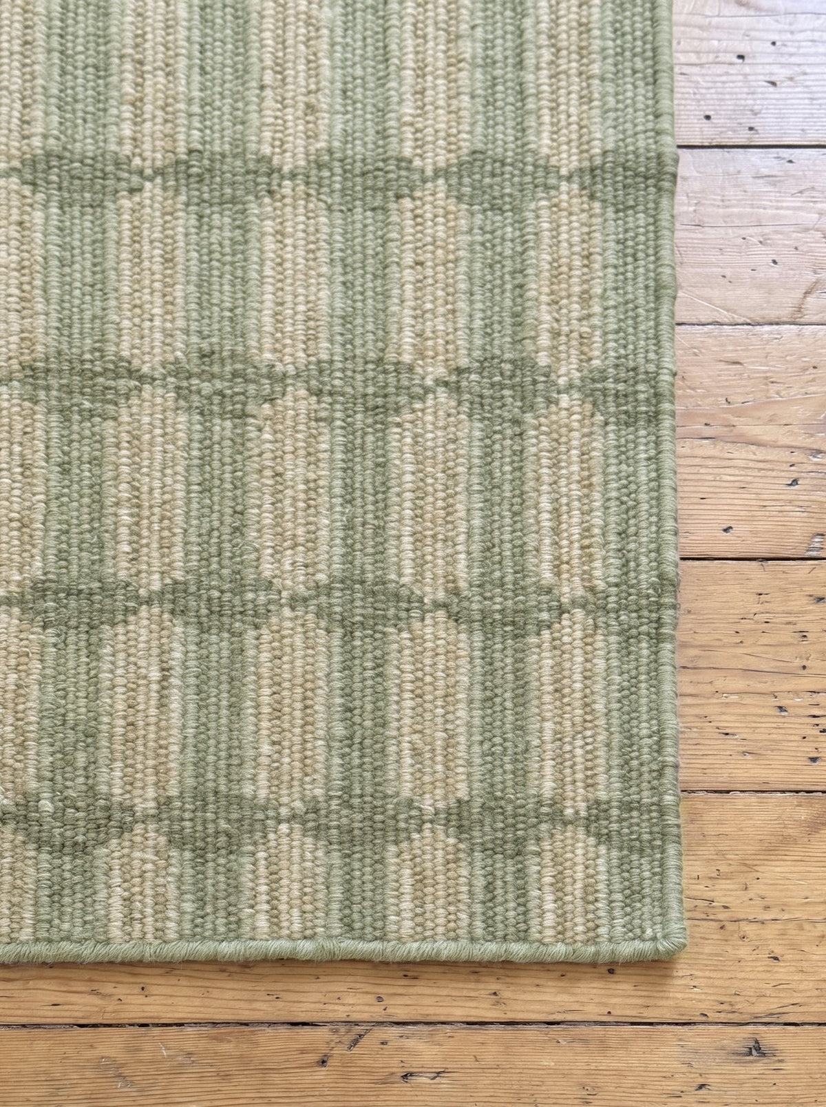 Corner of the Article 211 sage trellis stripe merino wool flatweave rug showing the weave and finished edge