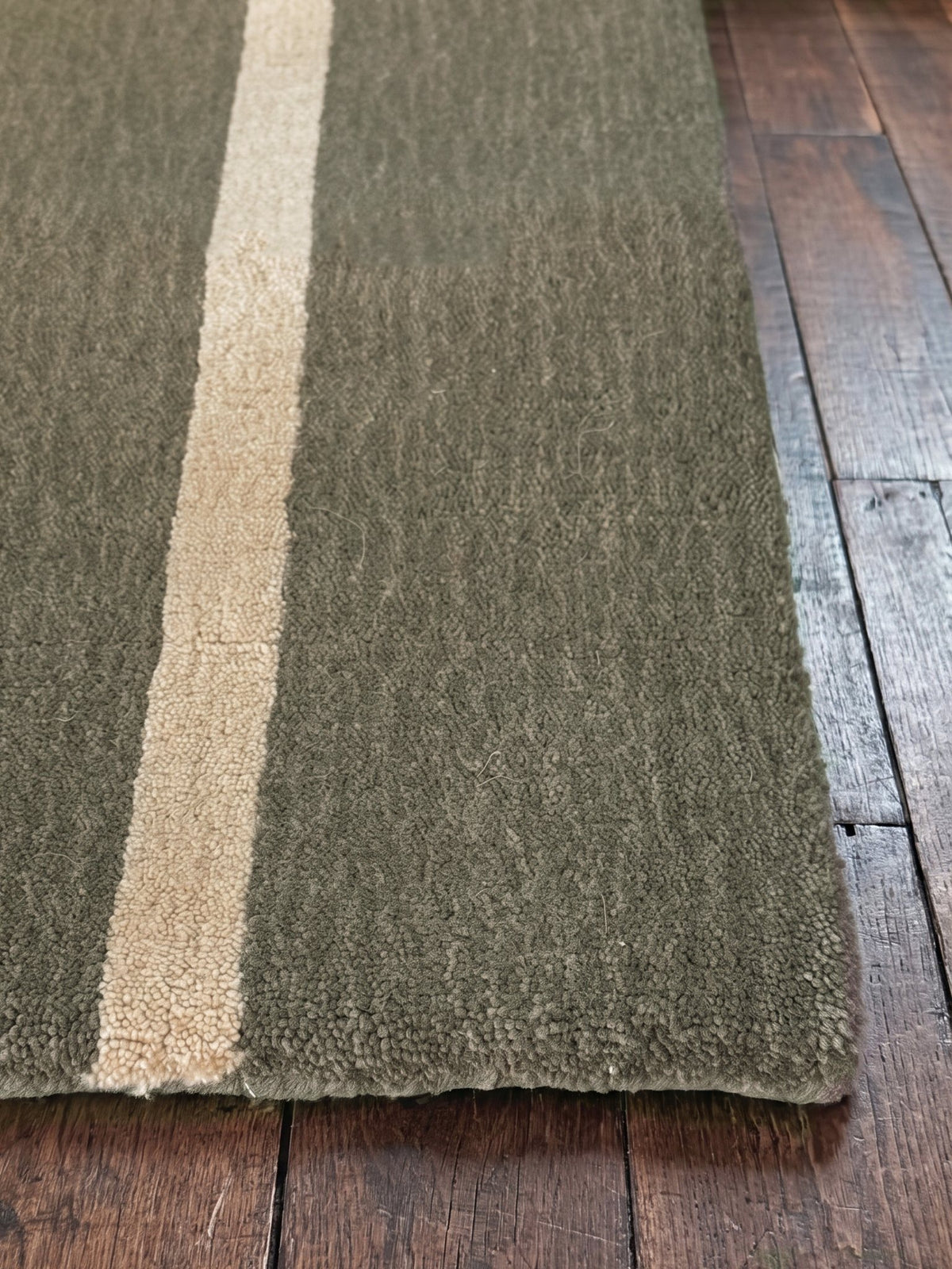 Corner of the Article 221 olive pinstripe merino wool and cashmere hand-loomed rug showing the pile and finished edge